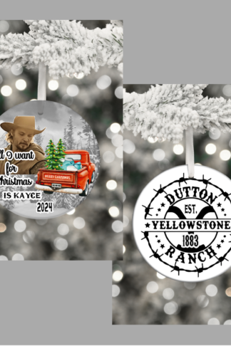 "Round ceramic ornament featuring Kayce Dutton from Yellowstone, with a rugged Western look and cowboy hat. The background showcases the Red Christmas Truck and the Yellowstone Mountains. On the other side is the Yellowstone Ranch the iconic 'Y' brand logo. And in bold Western-style lettering, it reads 'All I Want for Christmas is Kayce.' Edged with subtle holiday touches like holly leaves and pinecones, the ornament hangs with a red ribbon or leather string, blending holiday cheer with rustic ranch vibes."
