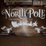 Handpainted stained solid pine wood Christmas sign reading “North Pole Trading Company” in vintage-style festive lettering.