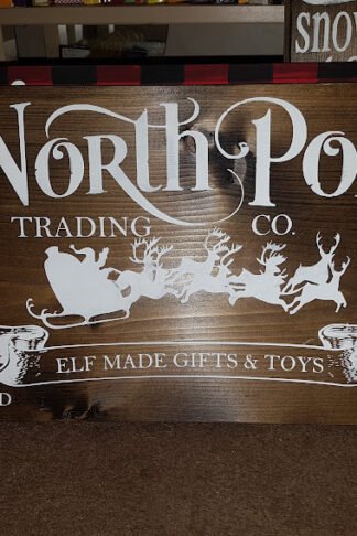 Handpainted stained solid pine wood Christmas sign reading “North Pole Trading Company” in vintage-style festive lettering.
